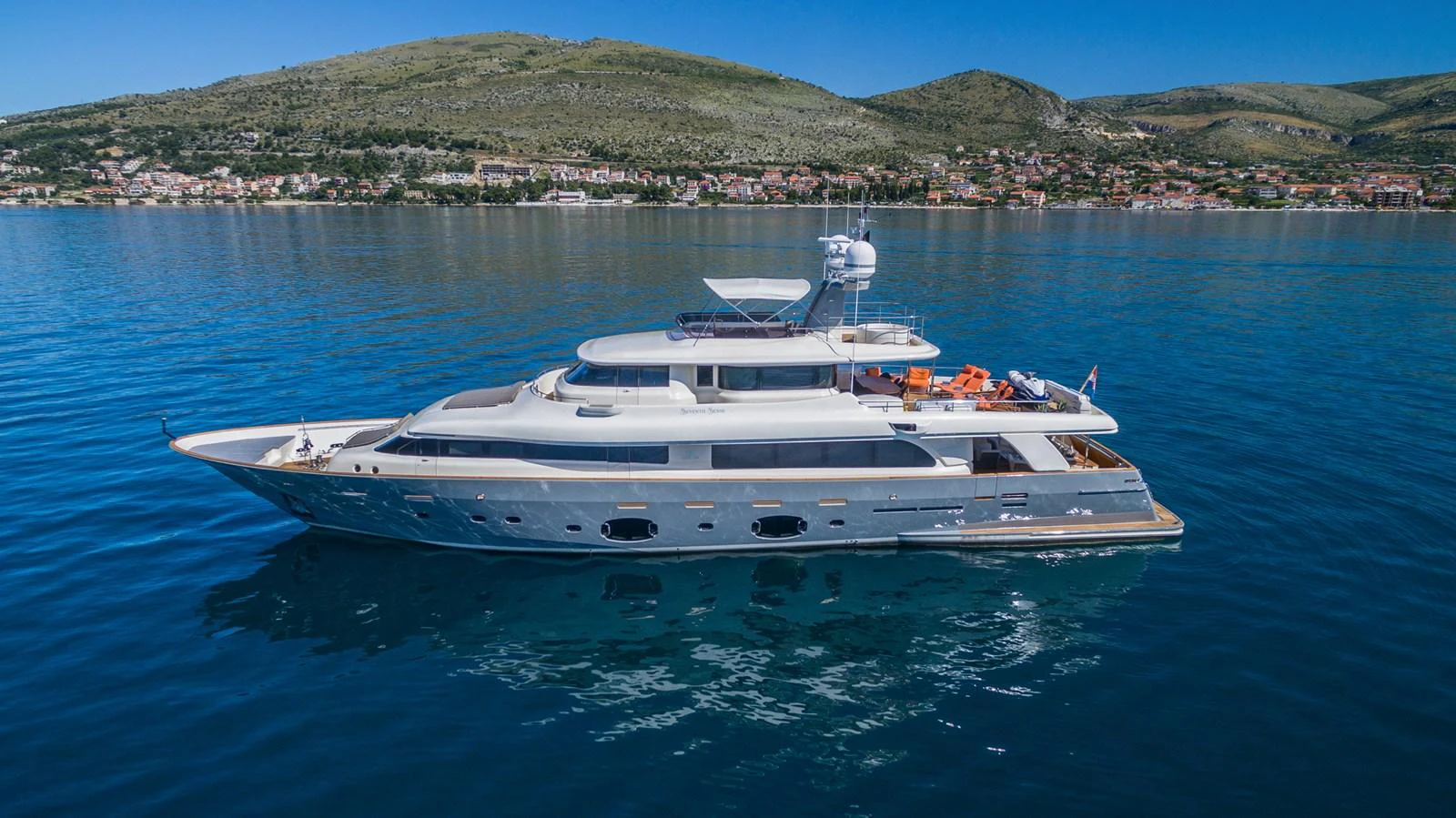 A sleek and elegant yacht glides on calm waters with a scenic coastal backdrop. aboard SEVENTH SENSE Yacht for Sale