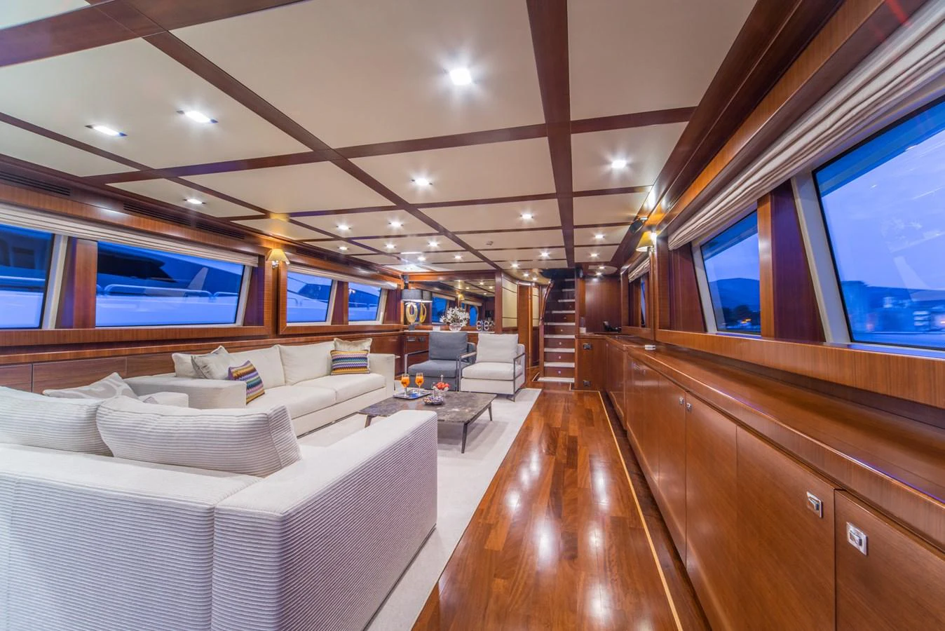 The spacious salon features luxurious seating and elegant wood finishes, creating a warm and inviting atmosphere. aboard SEVENTH SENSE Yacht for Sale