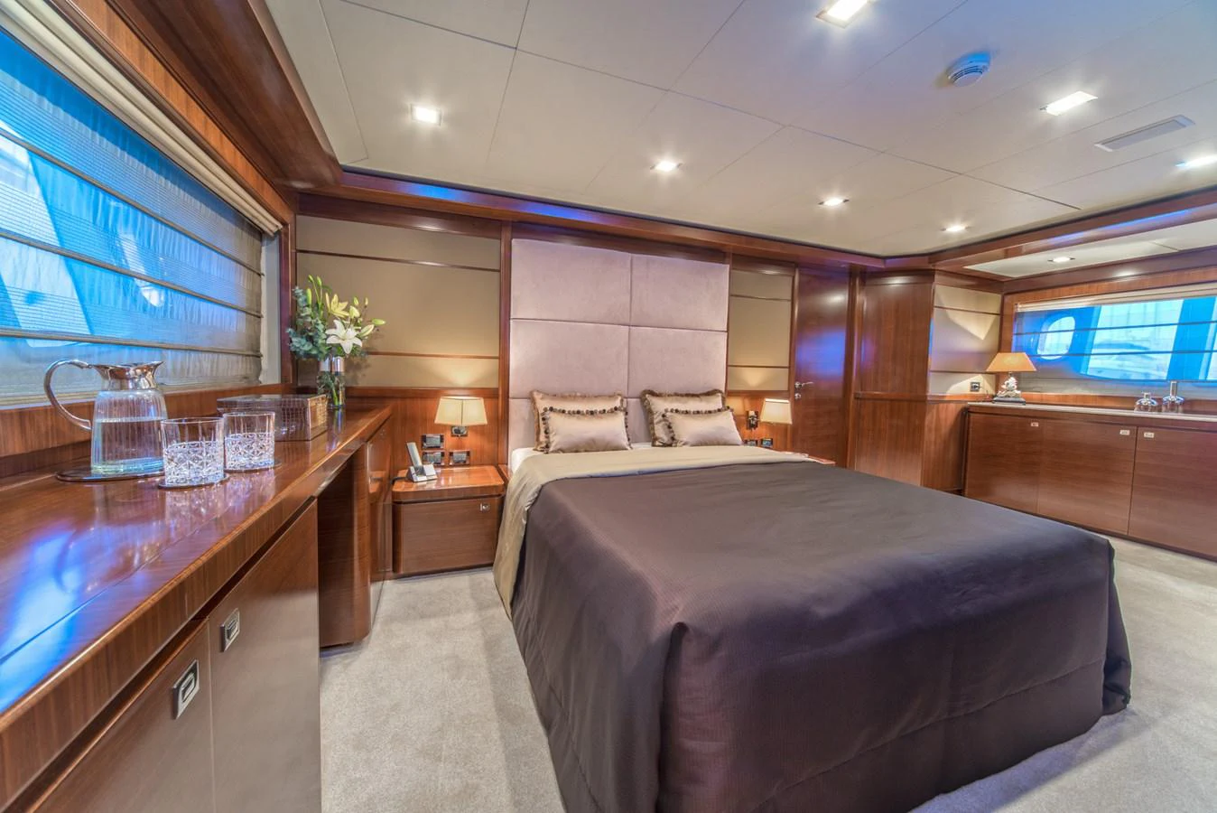 The master stateroom features a luxurious bed with elegant wood paneling and ample natural light. aboard SEVENTH SENSE Yacht for Sale