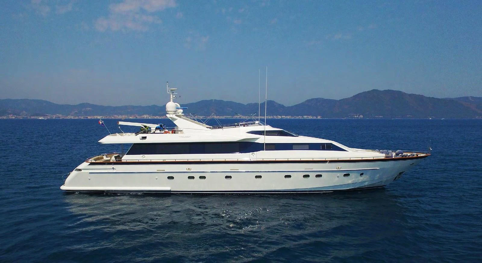 A sleek and elegant yacht cruising on calm waters with a scenic mountainous backdrop. aboard Q Yacht for Sale