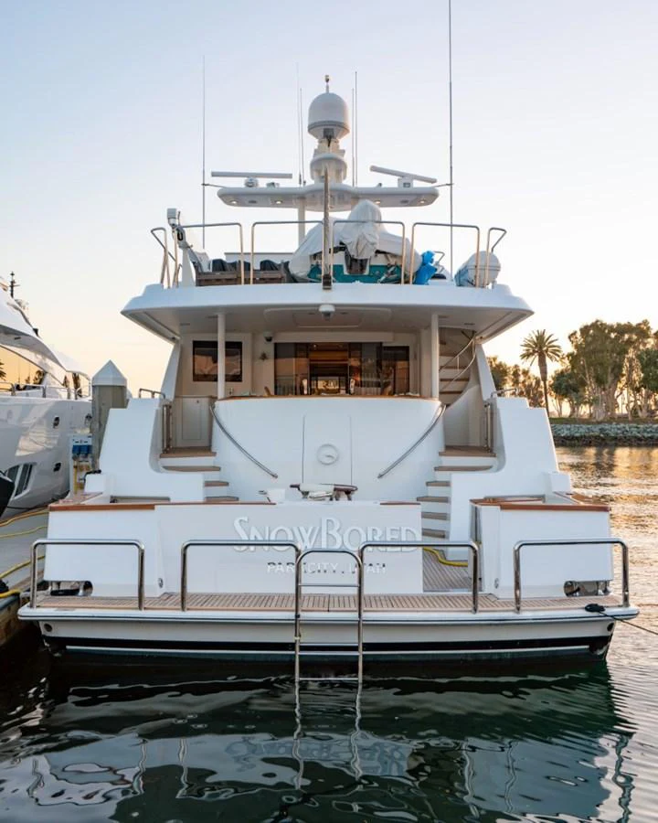 The yacht is docked at a marina, showcasing its stern with elegant steps leading up to the main deck. aboard SNOWBORED Yacht for Sale