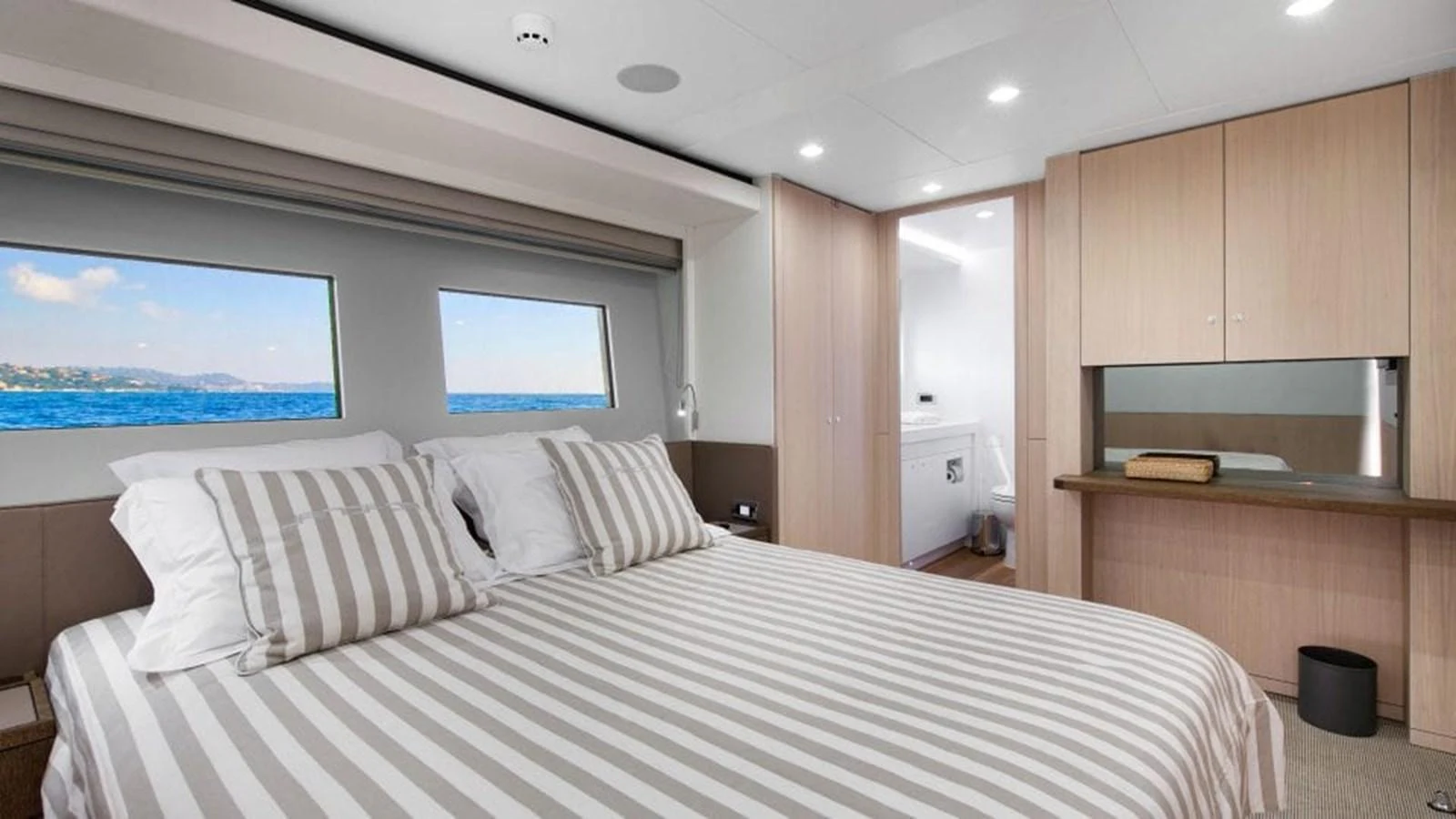 The stateroom features a comfortable bed with striped linens and large windows offering a stunning sea view. aboard JANGADA Yacht for Sale