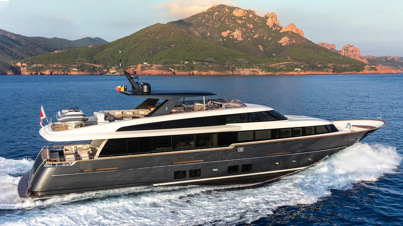 A sleek and modern yacht cruises through the water with a scenic mountainous backdrop. aboard JANGADA Yacht for Sale