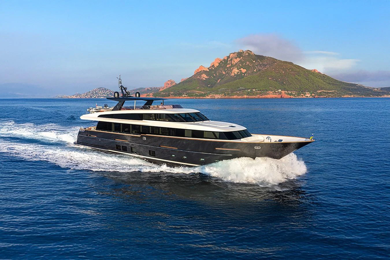 A sleek, modern yacht cruising on open water with a scenic mountainous backdrop. aboard JANGADA Yacht for Sale