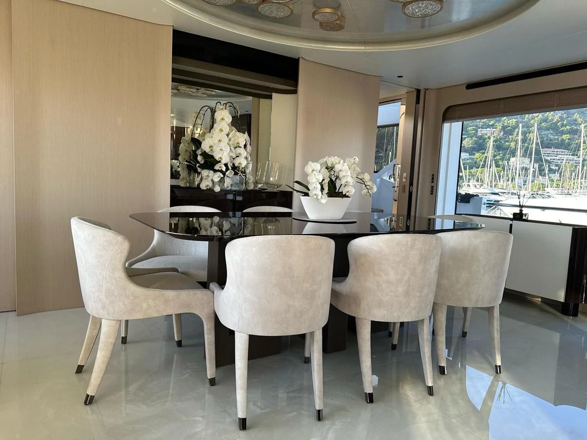 The yacht's dining area features a sleek glass table surrounded by plush, modern chairs, with a scenic view through the windows. aboard G Yacht for Sale