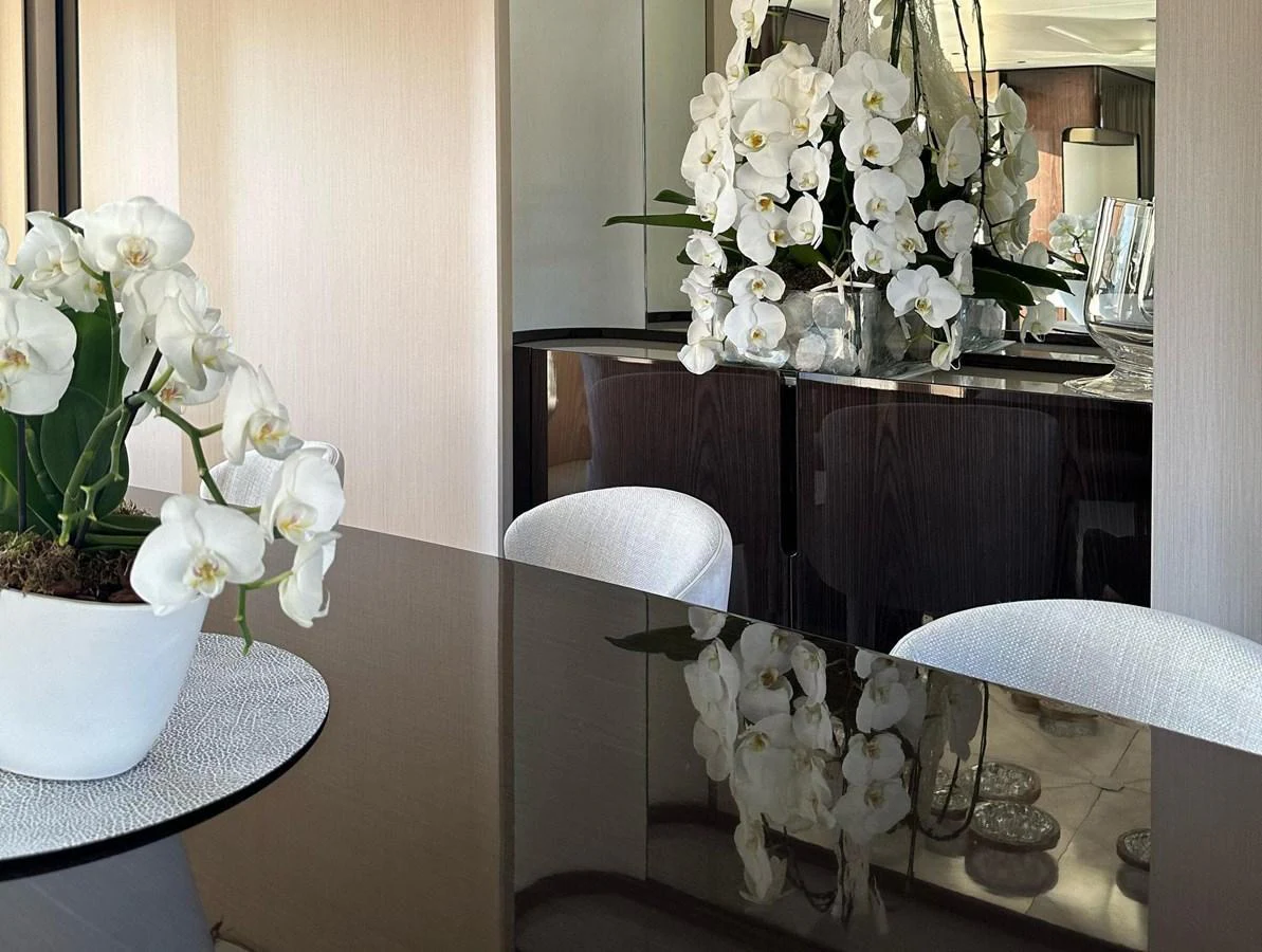 The yacht's interior features elegant decor with white orchids and a reflective dining table. aboard G Yacht for Sale