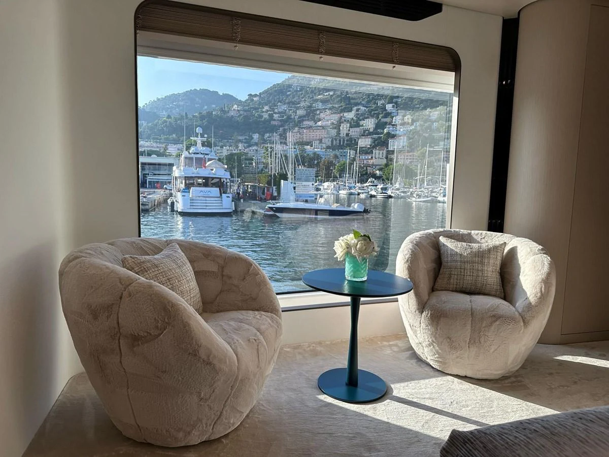 The yacht's interior features a cozy seating area with plush chairs and a table, offering a picturesque view of the marina through a large window. aboard G Yacht for Sale