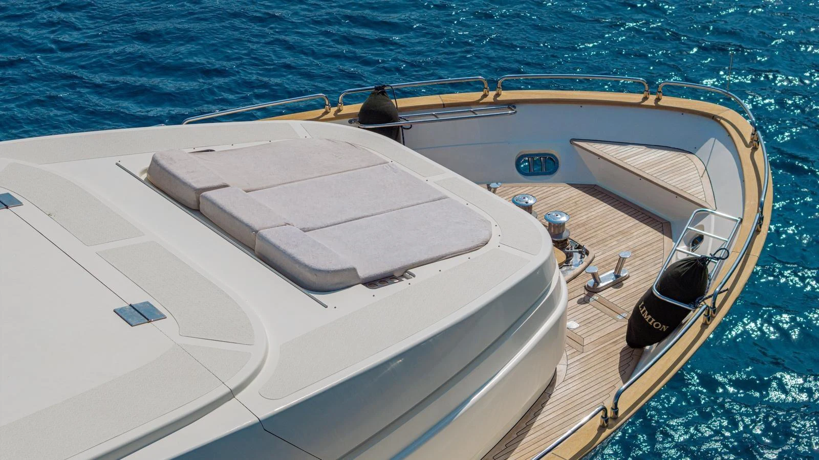 The foredeck of the yacht features a spacious sunpad and sleek design elements, set against the backdrop of clear blue waters. aboard LIMION Yacht for Sale