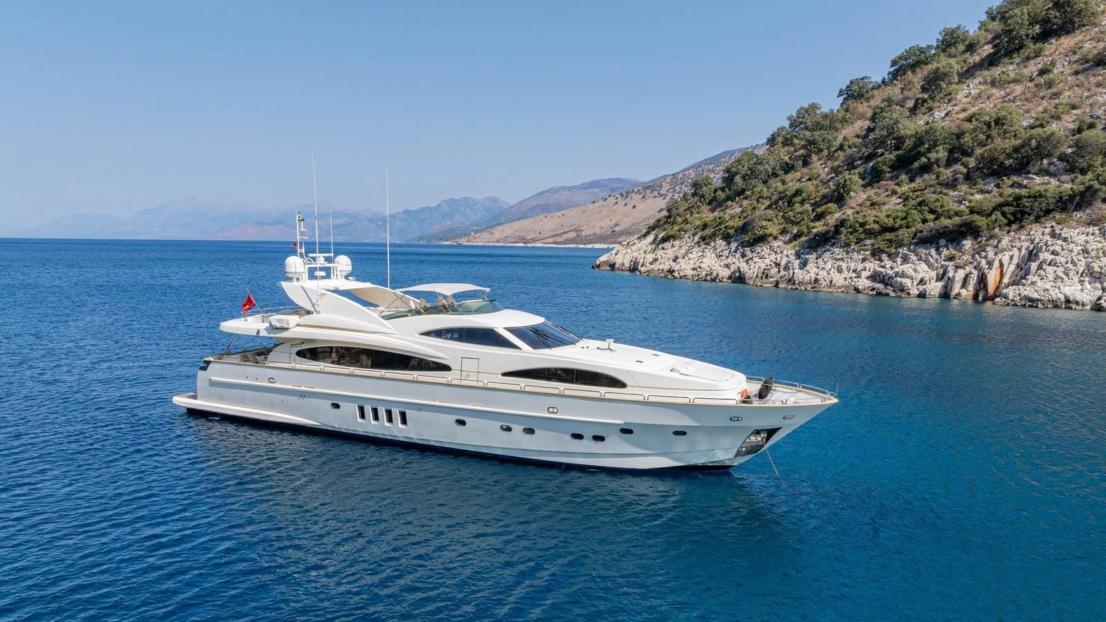 A sleek and elegant yacht cruising along a picturesque coastline under clear blue skies. aboard LIMION Yacht for Sale