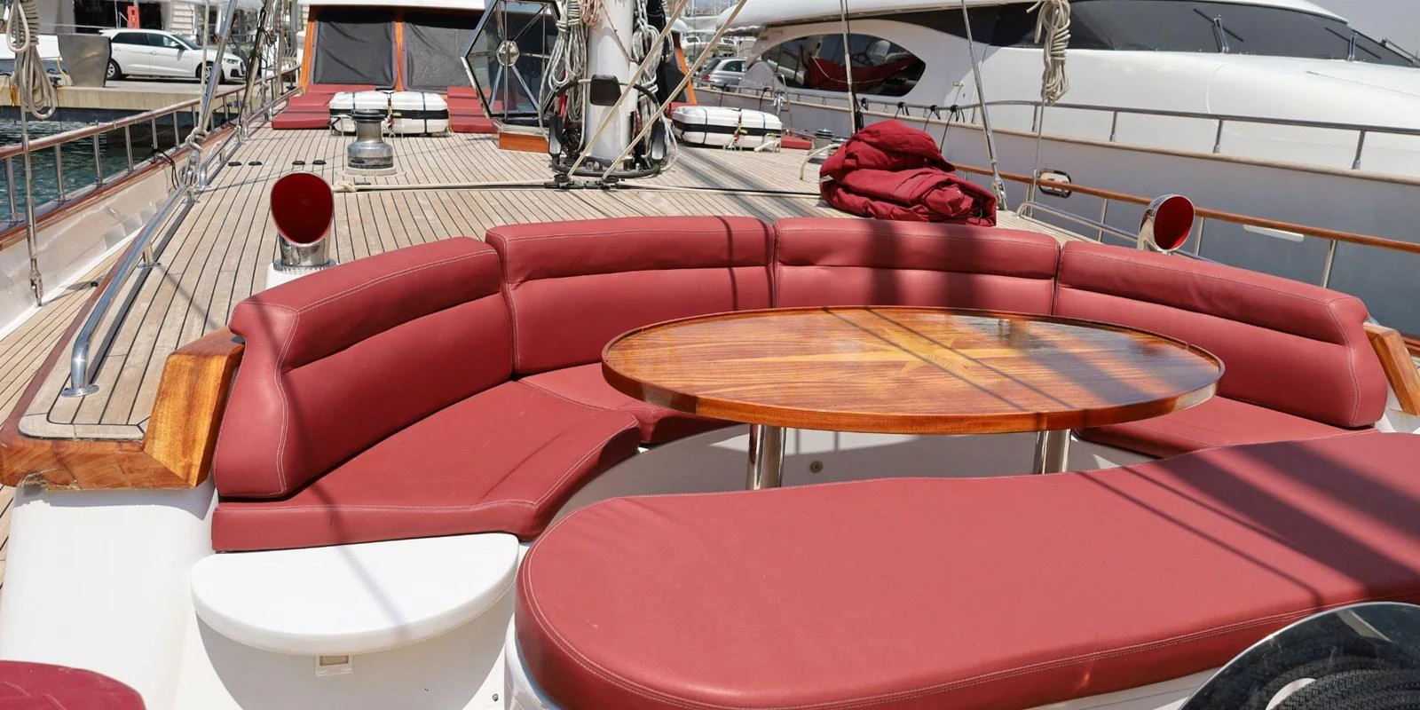 The yacht's aft deck features a spacious seating area with red cushions and a wooden table, perfect for outdoor relaxation and dining. aboard AKHENATON Yacht for Sale