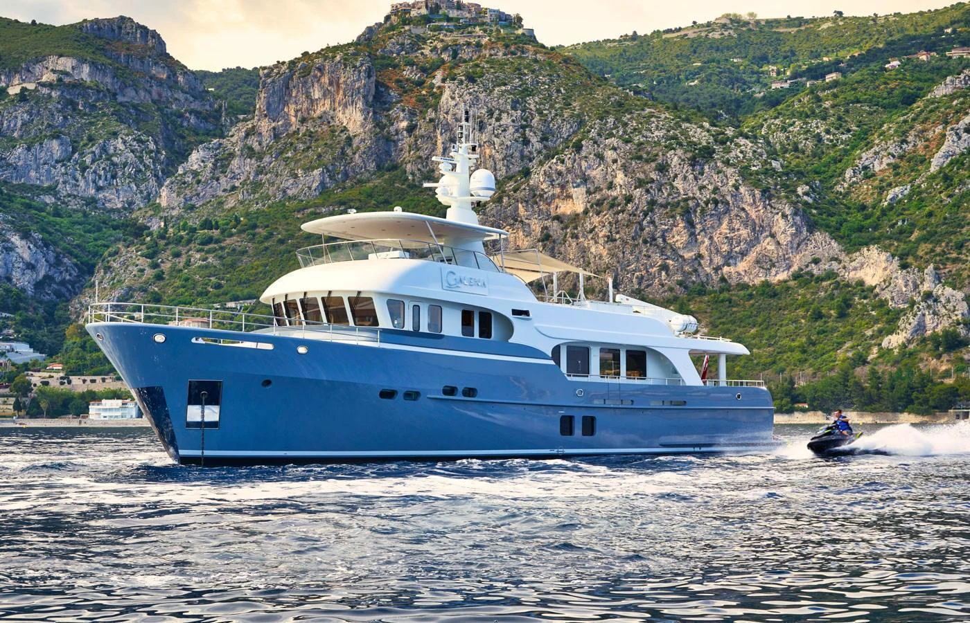 A luxurious yacht cruises through scenic waters with a jet ski speeding alongside. aboard GALENA Yacht for Sale