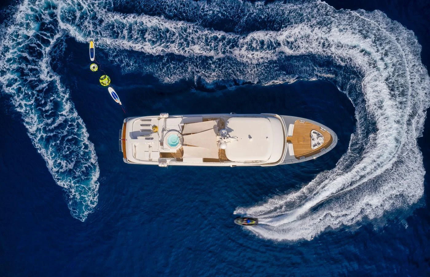 An aerial view of a luxurious yacht cruising through deep blue waters, surrounded by water toys and a jet ski. aboard GALENA Yacht for Sale