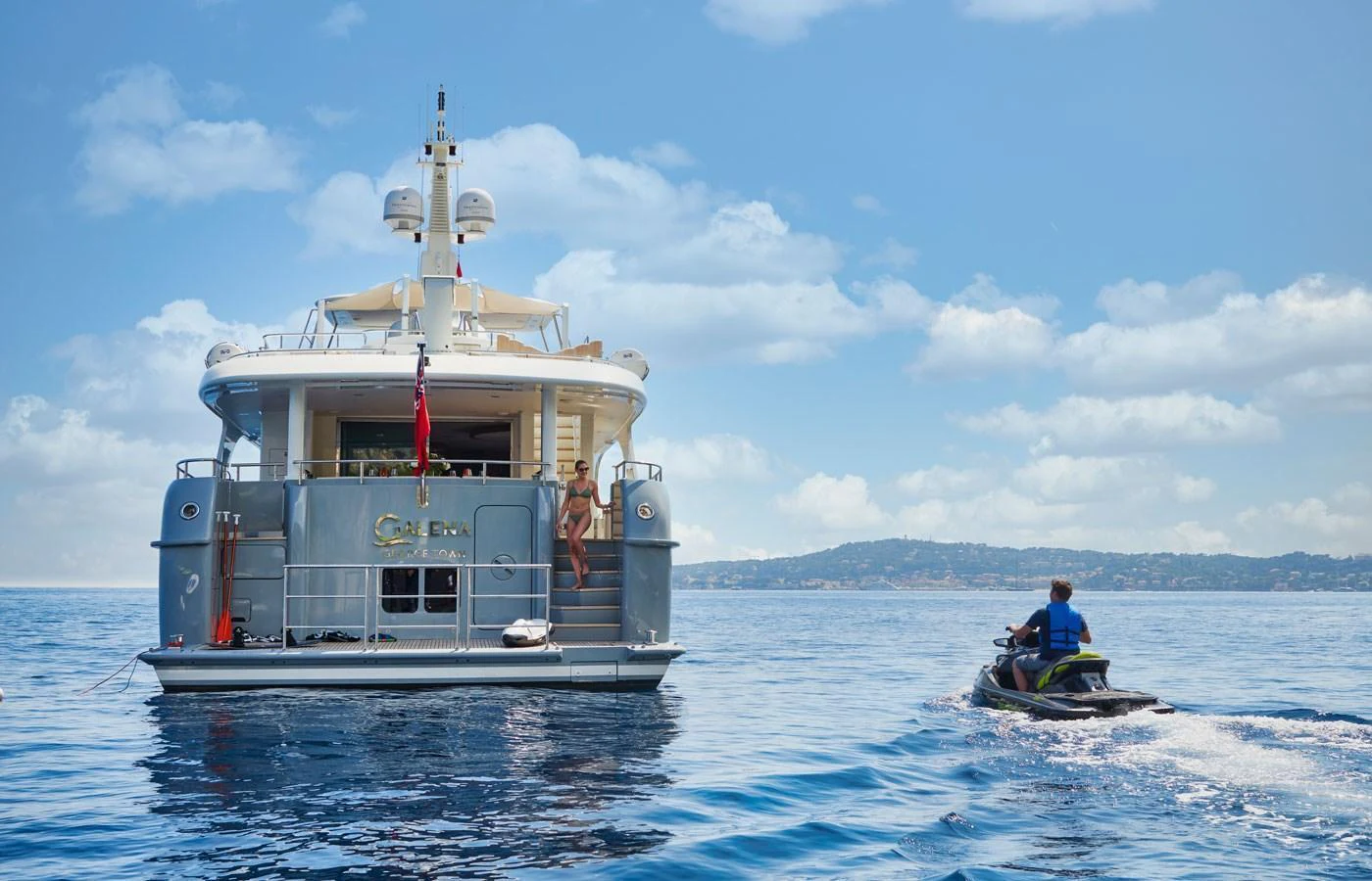 A luxurious yacht is anchored in calm waters with a person riding a jet ski nearby. aboard GALENA Yacht for Sale
