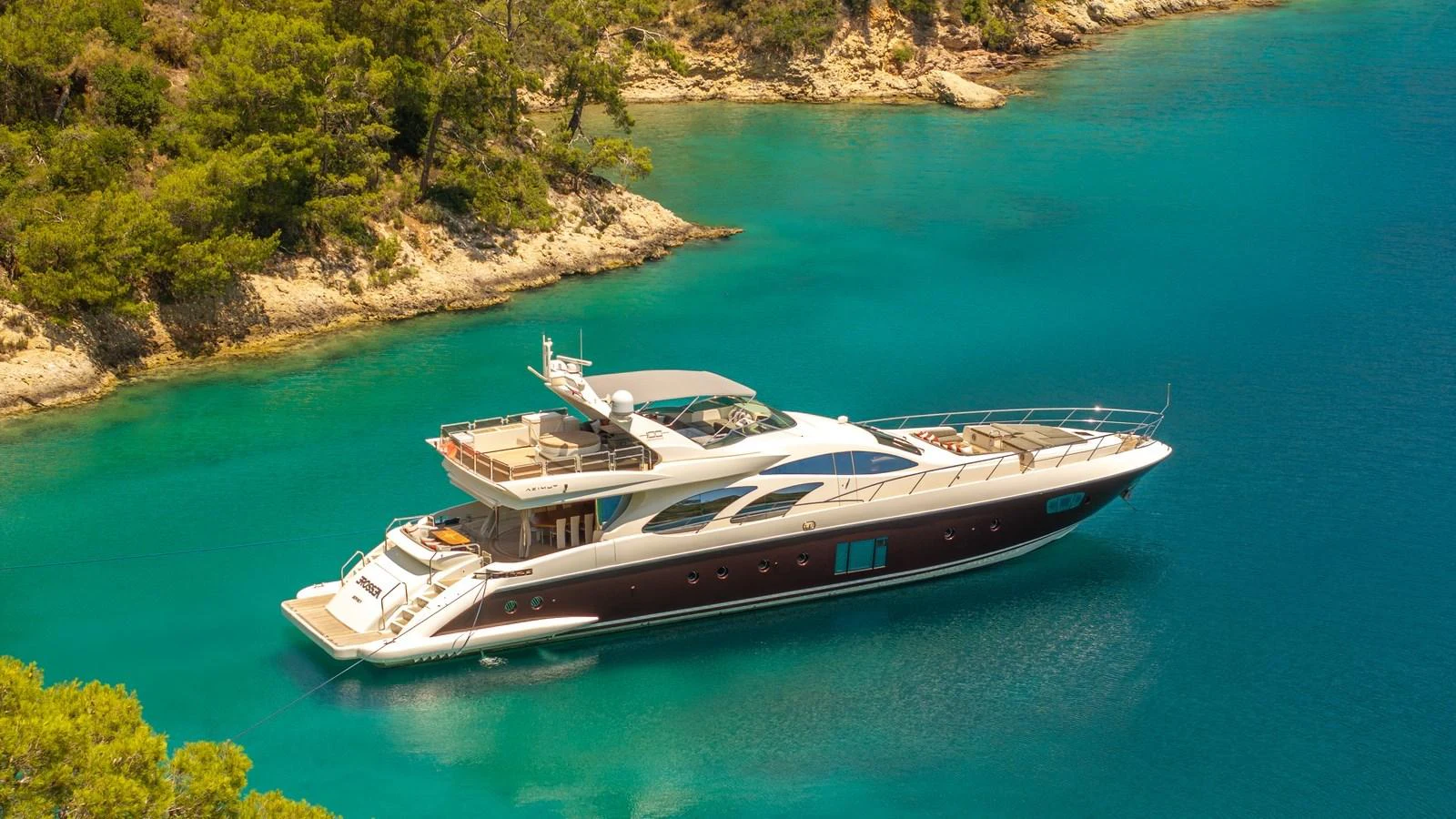 A sleek yacht is anchored in a serene, turquoise bay surrounded by lush greenery. aboard EROSSEA Yacht for Sale