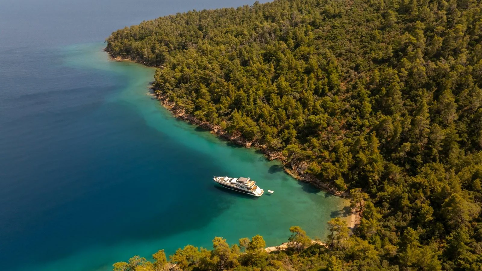 A luxurious yacht is anchored in a serene, secluded cove surrounded by lush greenery and clear blue waters. aboard EROSSEA Yacht for Sale
