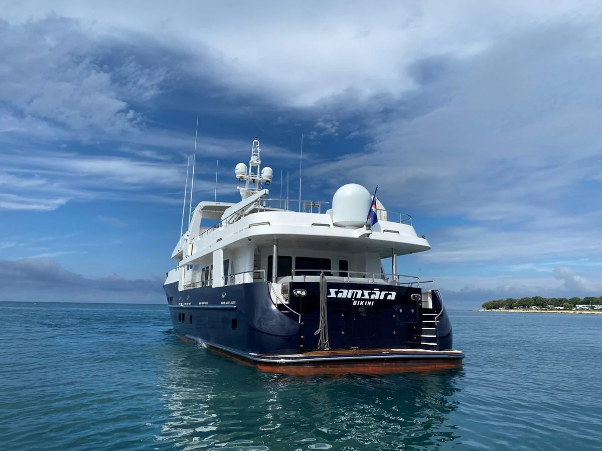 A luxurious yacht is anchored in calm, clear waters under a partly cloudy sky. aboard SAMSARA Yacht for Sale