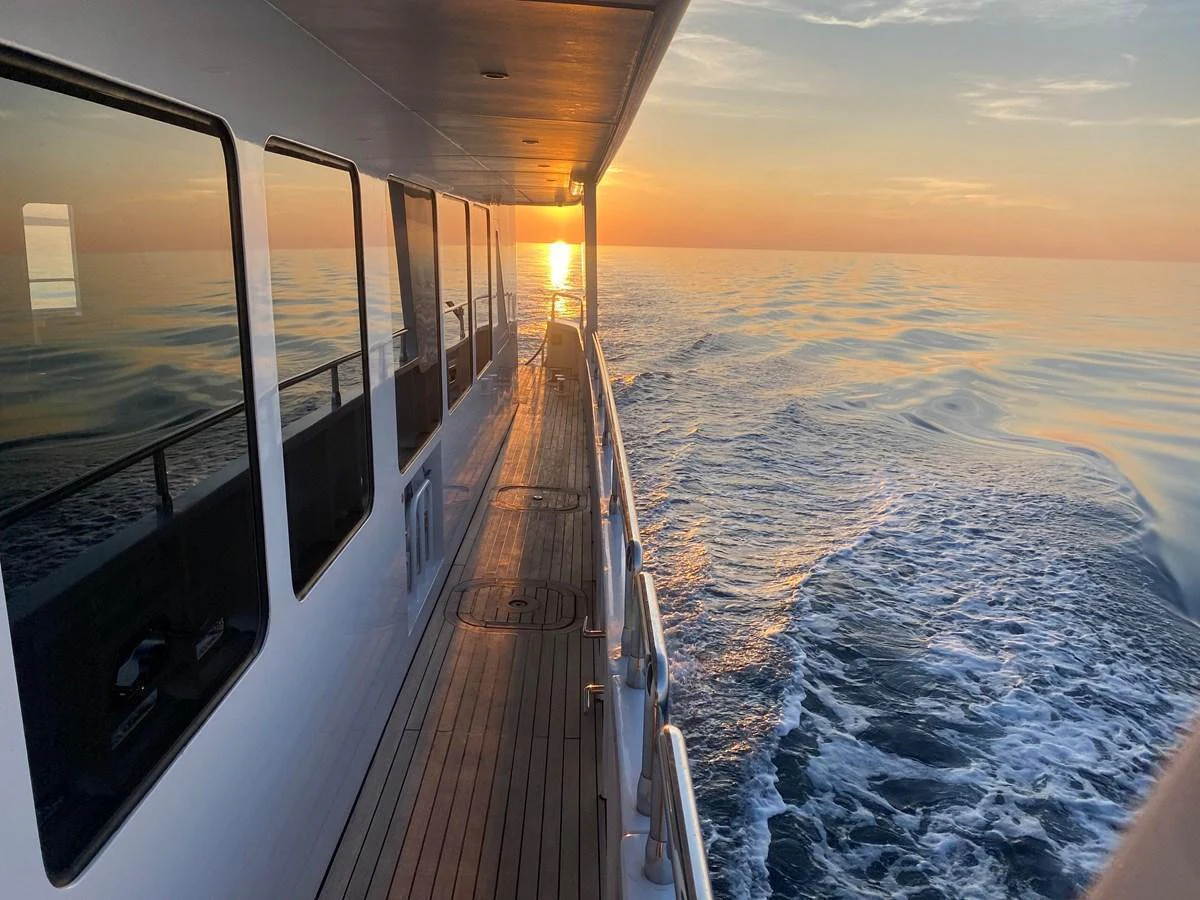 The yacht's side deck offers a serene view of the sunset over calm waters. aboard SAMSARA Yacht for Sale