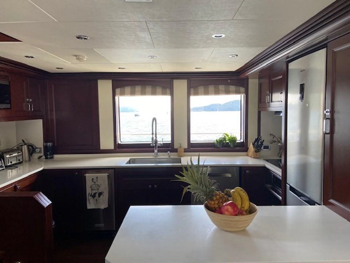 The galley features modern appliances and a large island with a bowl of fresh fruit, framed by large windows offering a scenic view. aboard SAMSARA Yacht for Sale