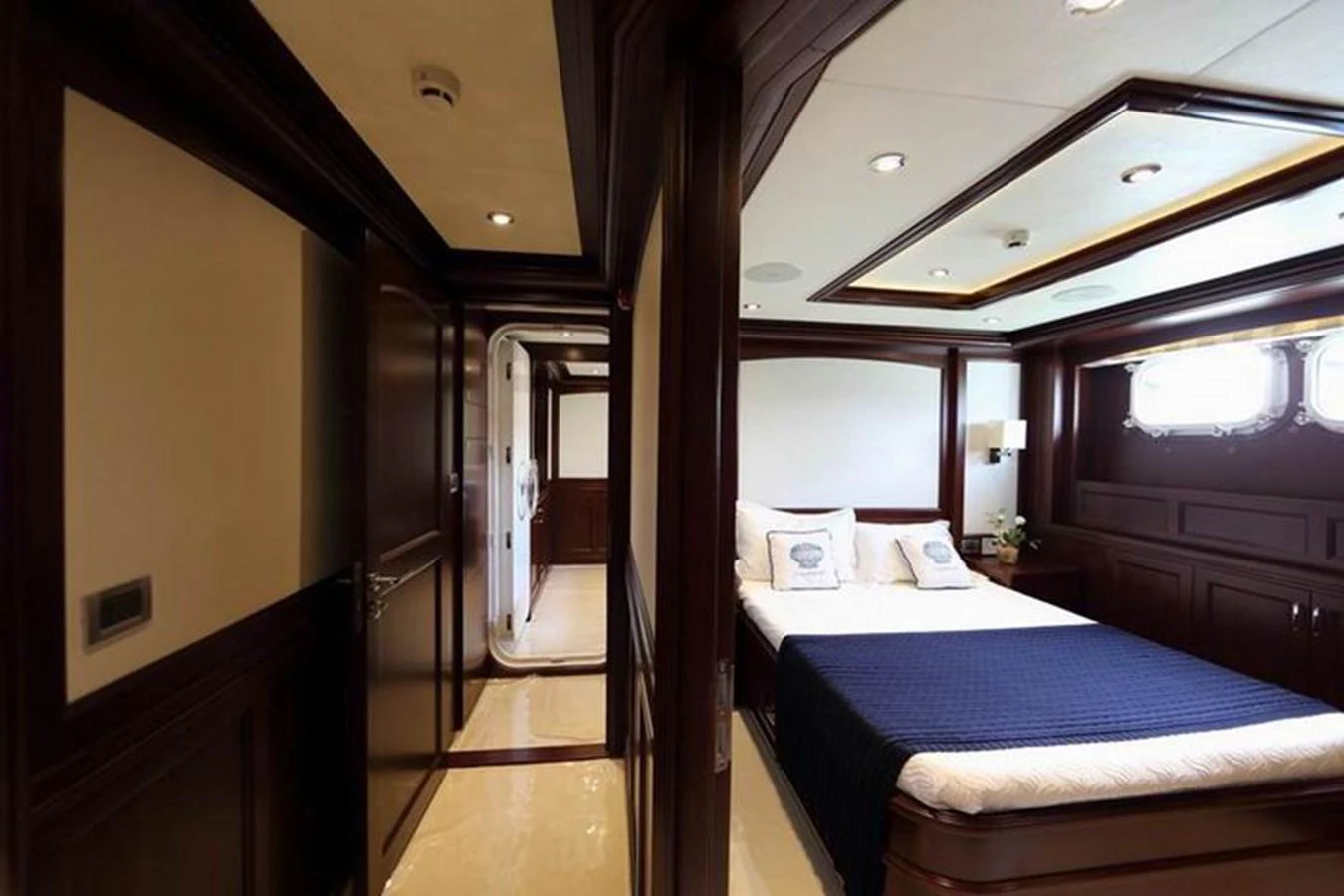 The stateroom features a luxurious bed with elegant wood paneling and ample natural light. aboard SAMSARA Yacht for Sale