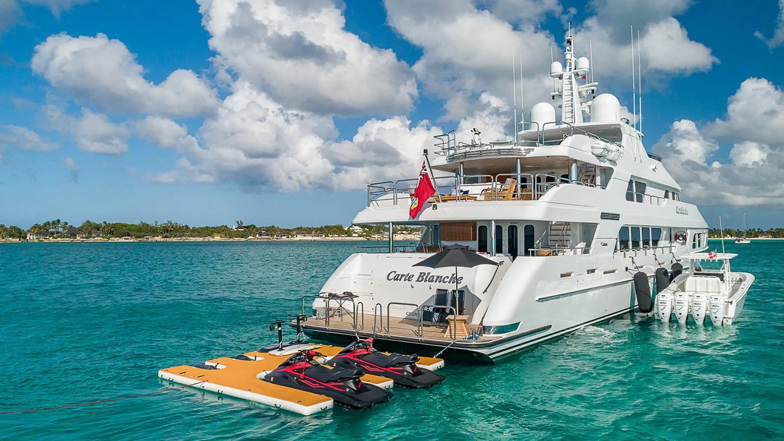The yacht is anchored in a serene turquoise sea, showcasing its spacious aft deck and water toys. aboard CARTE BLANCHE Yacht for Sale