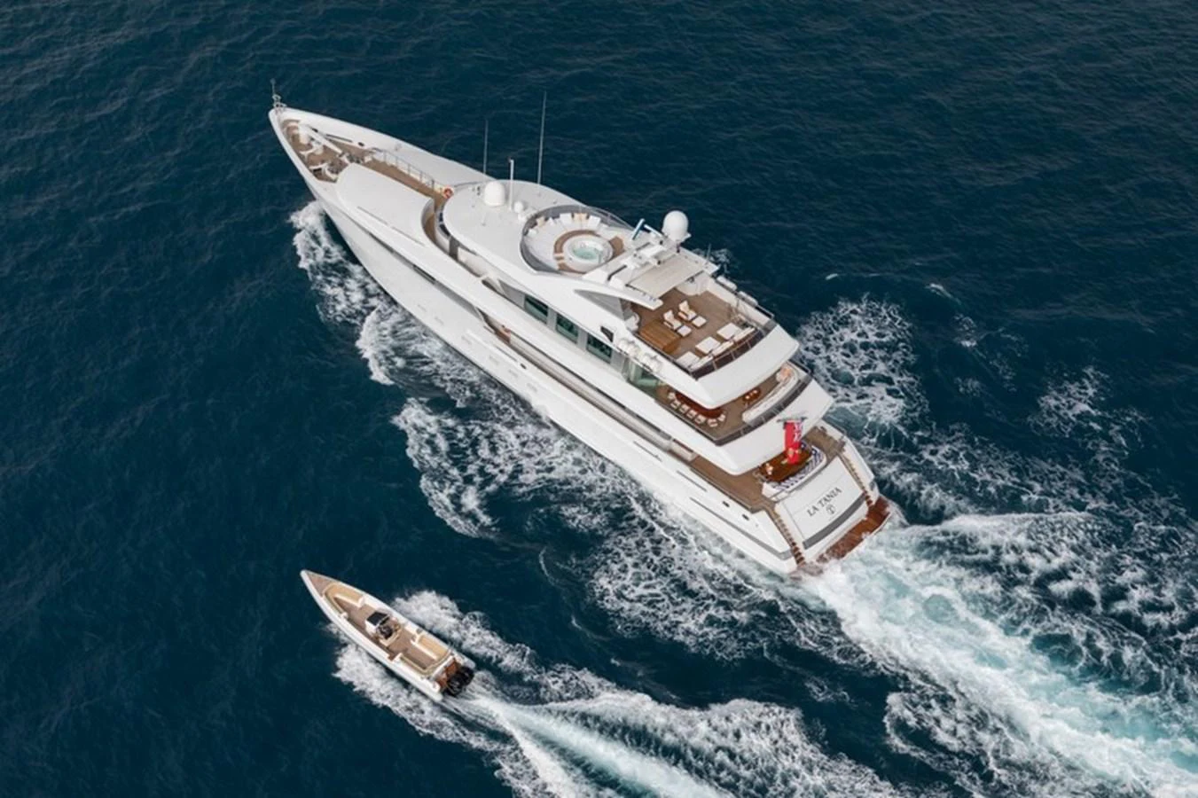 A luxurious yacht cruising through the open sea with a tender boat trailing behind. aboard LA TANIA Yacht for Sale