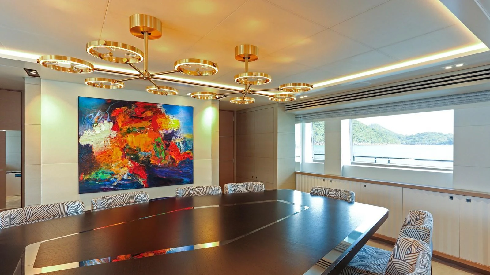 The yacht's dining area features a large table, modern lighting, and a vibrant piece of artwork. aboard HEESEN 47M Yacht for Sale