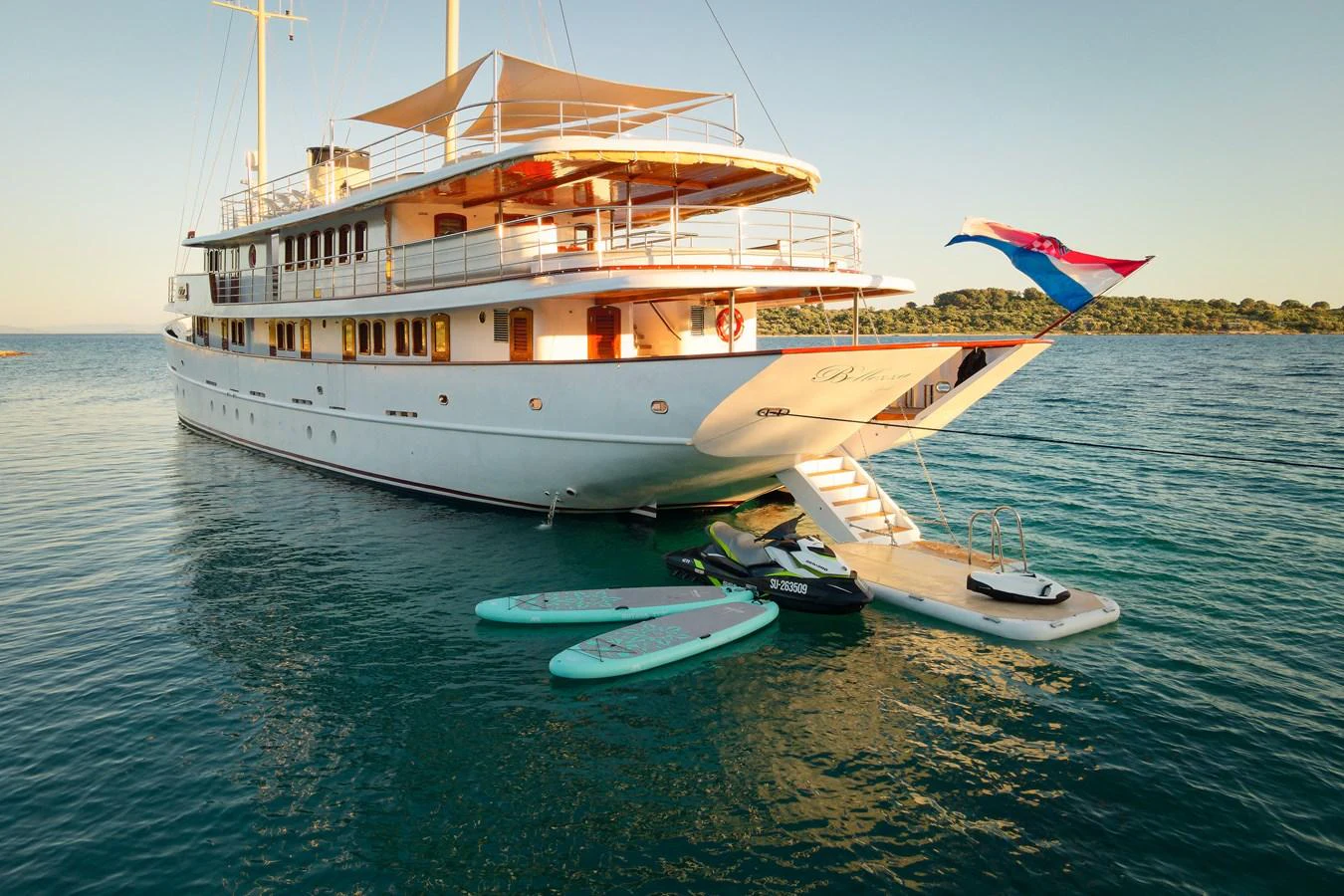 A luxurious yacht is anchored in calm waters, with paddleboards and a jet ski ready for adventure. aboard BELLEZZA Yacht for Sale