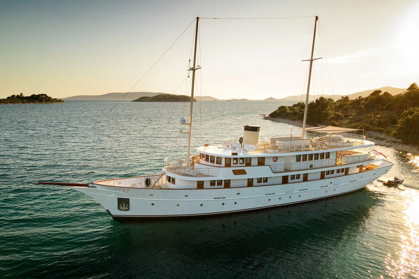 A classic yacht cruises gracefully along a serene coastline at sunset. aboard BELLEZZA Yacht for Sale
