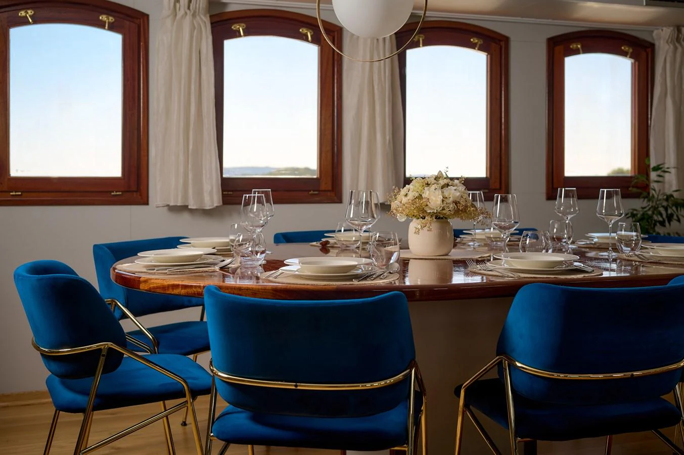 The yacht's dining area features an elegant table set for a meal, surrounded by plush blue chairs and illuminated by natural light through large windows. aboard BELLEZZA Yacht for Sale