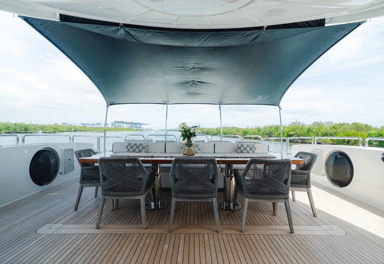 The aft deck features an elegant dining area with a large table and comfortable chairs under a shaded canopy. aboard BET ON IT Yacht for Sale