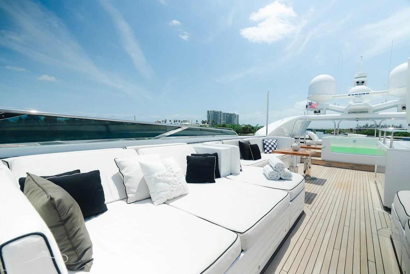 The sundeck features luxurious lounging areas with plush white cushions and a jacuzzi under a clear blue sky. aboard BET ON IT Yacht for Sale