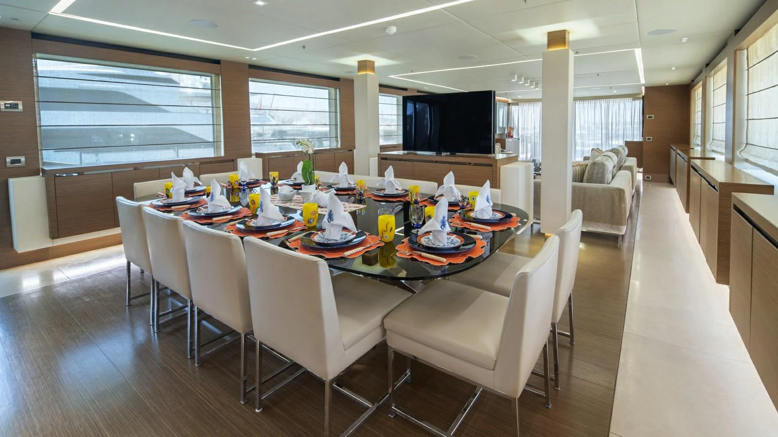 The yacht's dining area features a large table set for a formal meal, surrounded by comfortable chairs and adjacent to a spacious lounge area. aboard IPANEMAS Yacht for Sale