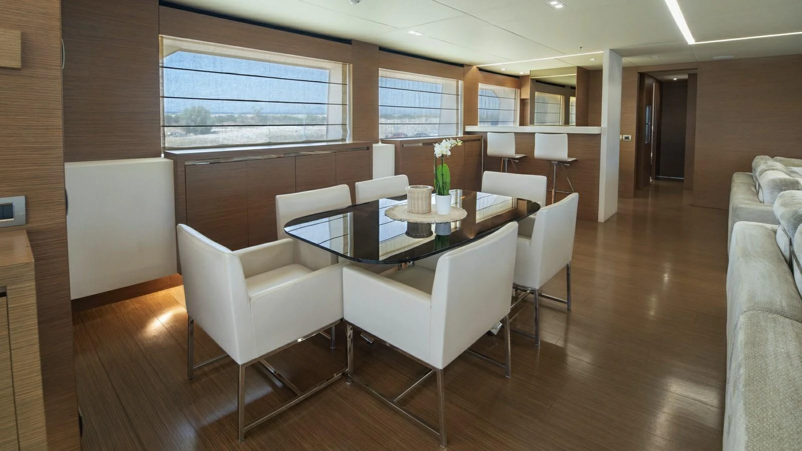 The yacht's dining area features a sleek glass table surrounded by modern white chairs, set against a backdrop of large windows offering panoramic views. aboard IPANEMAS Yacht for Sale