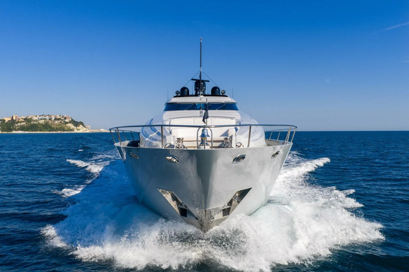 A sleek yacht cuts through the water with a stunning coastal backdrop. aboard FIVE Yacht for Sale