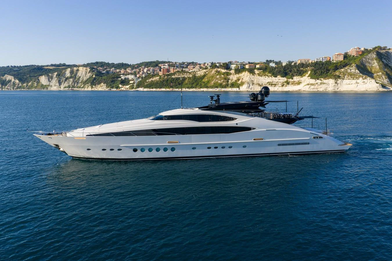 A sleek and modern yacht glides through calm waters with a scenic coastal backdrop. aboard FIVE Yacht for Sale