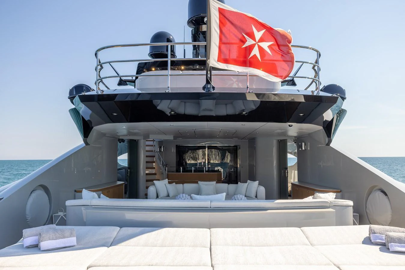 The yacht's aft deck features a spacious lounging area with plush seating and a flag proudly displayed. aboard FIVE Yacht for Sale