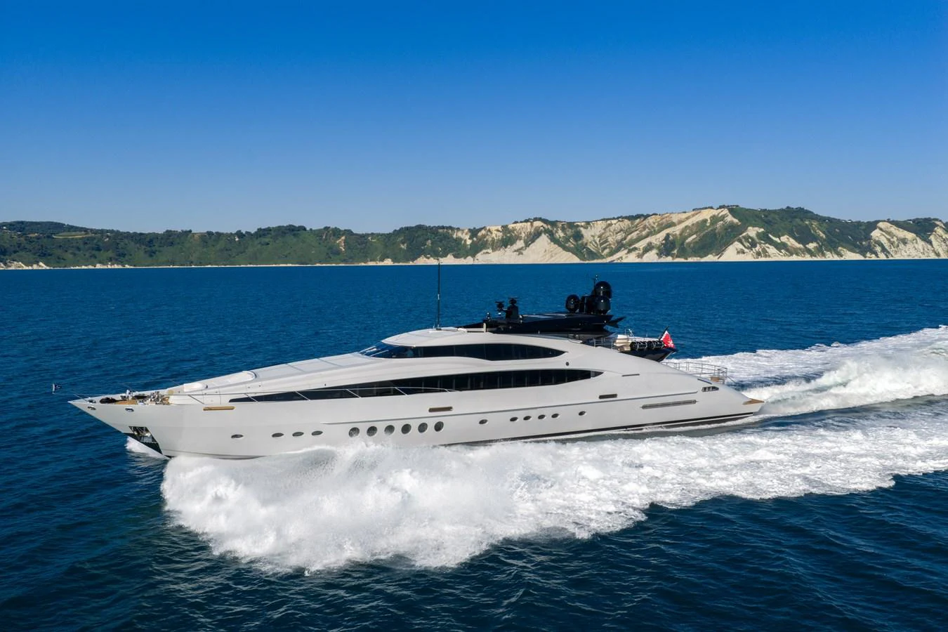 A sleek and modern yacht cruises swiftly through the open water, set against a backdrop of scenic coastal hills. aboard FIVE Yacht for Sale