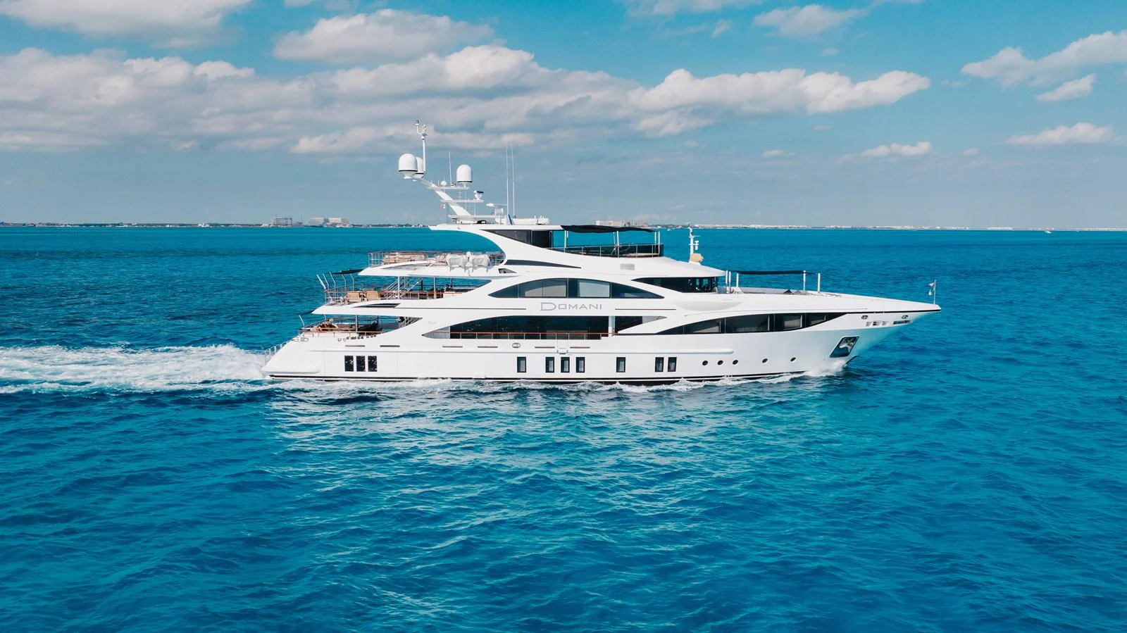 A luxurious yacht cruises through clear blue waters under a partly cloudy sky. aboard DOMANI Yacht for Sale
