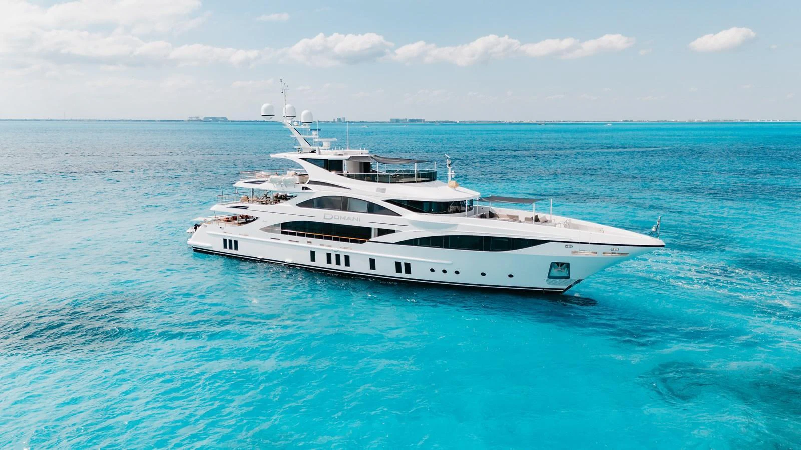 A luxurious yacht glides gracefully over crystal-clear turquoise waters under a bright blue sky. aboard DOMANI Yacht for Sale
