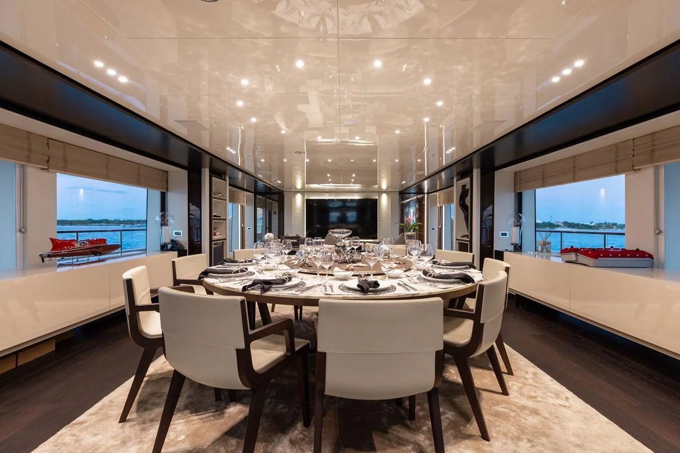 The elegant dining area features a large table set for a formal meal, surrounded by comfortable chairs and panoramic windows offering stunning views. aboard DOMANI Yacht for Sale