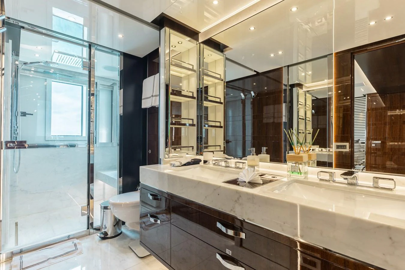 The yacht's bathroom features a luxurious double sink vanity with a modern glass-enclosed shower. aboard DOMANI Yacht for Sale