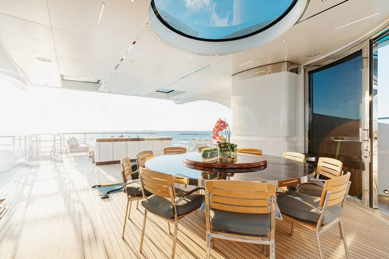 The aft deck features a spacious dining area with a round table and comfortable chairs, perfect for alfresco dining. aboard DOMANI Yacht for Sale