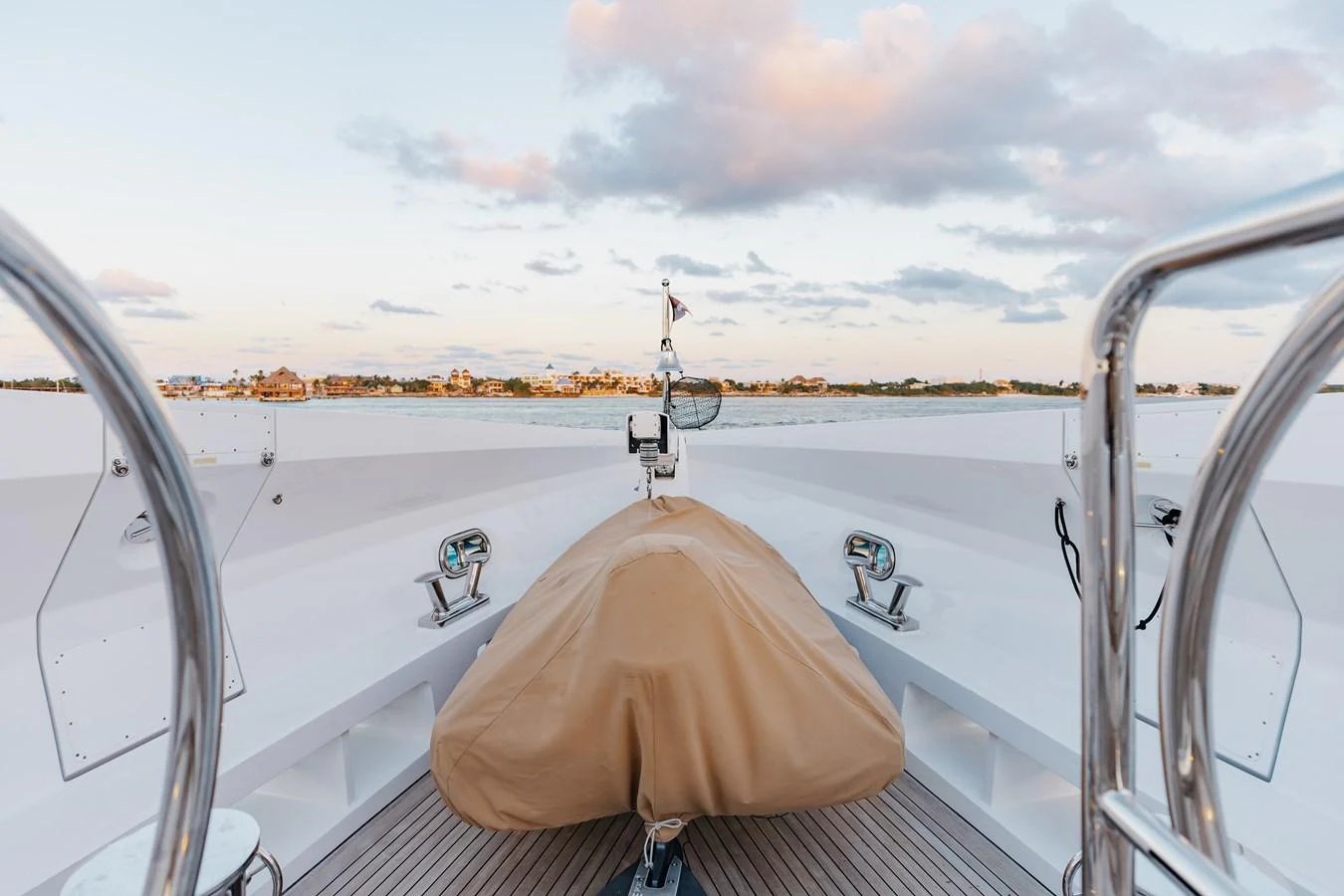 The bow of the yacht features a covered anchor winch and polished metal railings, set against a serene waterfront backdrop. aboard DOMANI Yacht for Sale