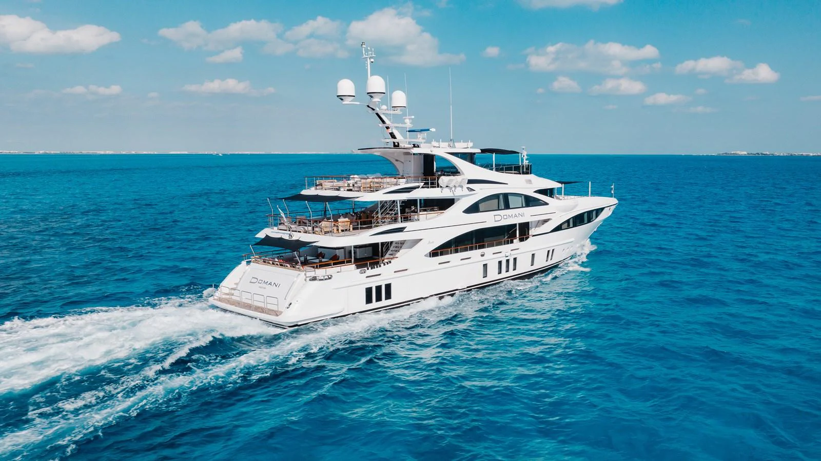 A luxurious yacht cruises through the open sea under a clear blue sky. aboard DOMANI Yacht for Sale