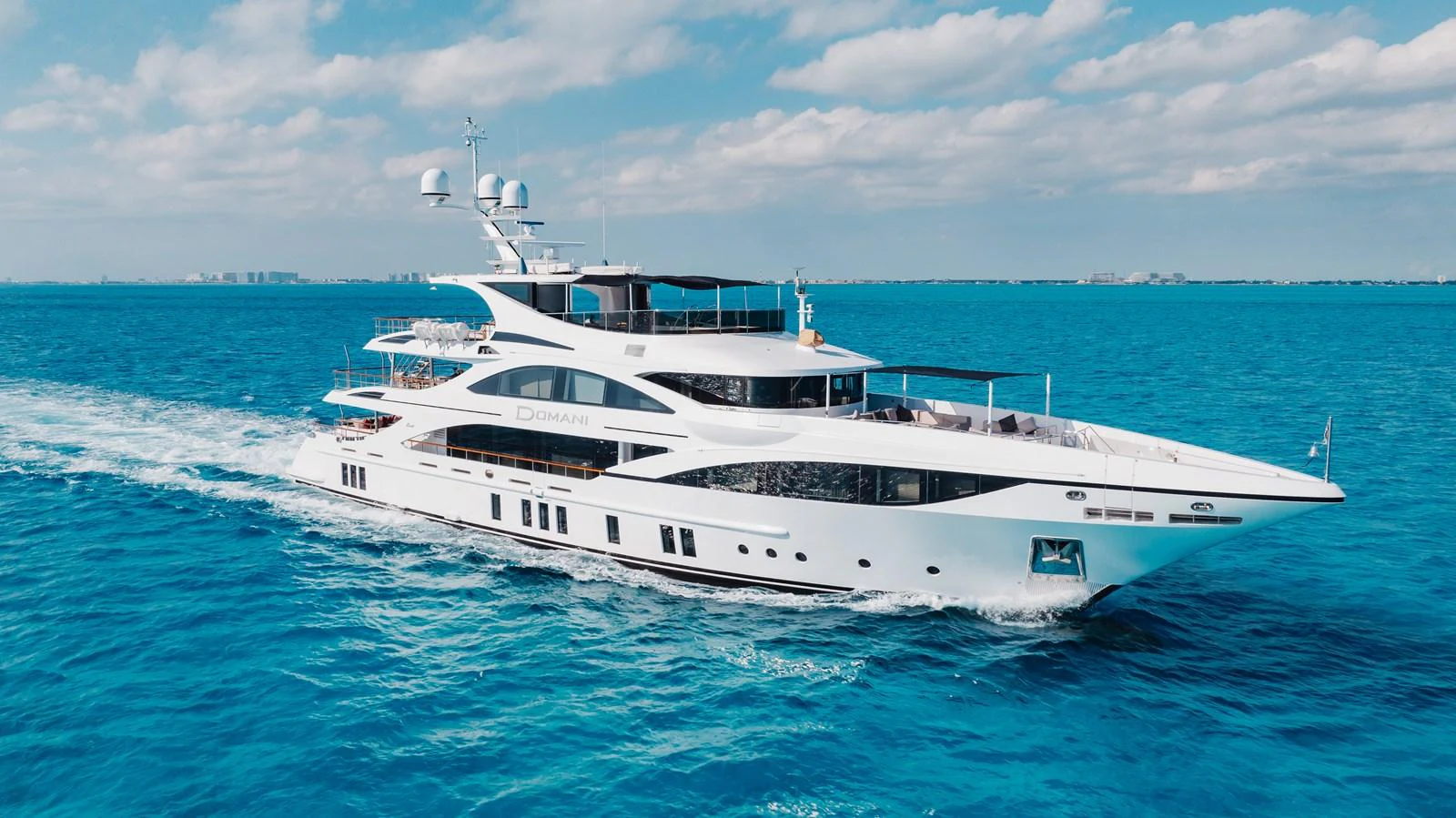 A sleek and modern yacht cruising through clear blue waters under a bright sky. aboard DOMANI Yacht for Sale