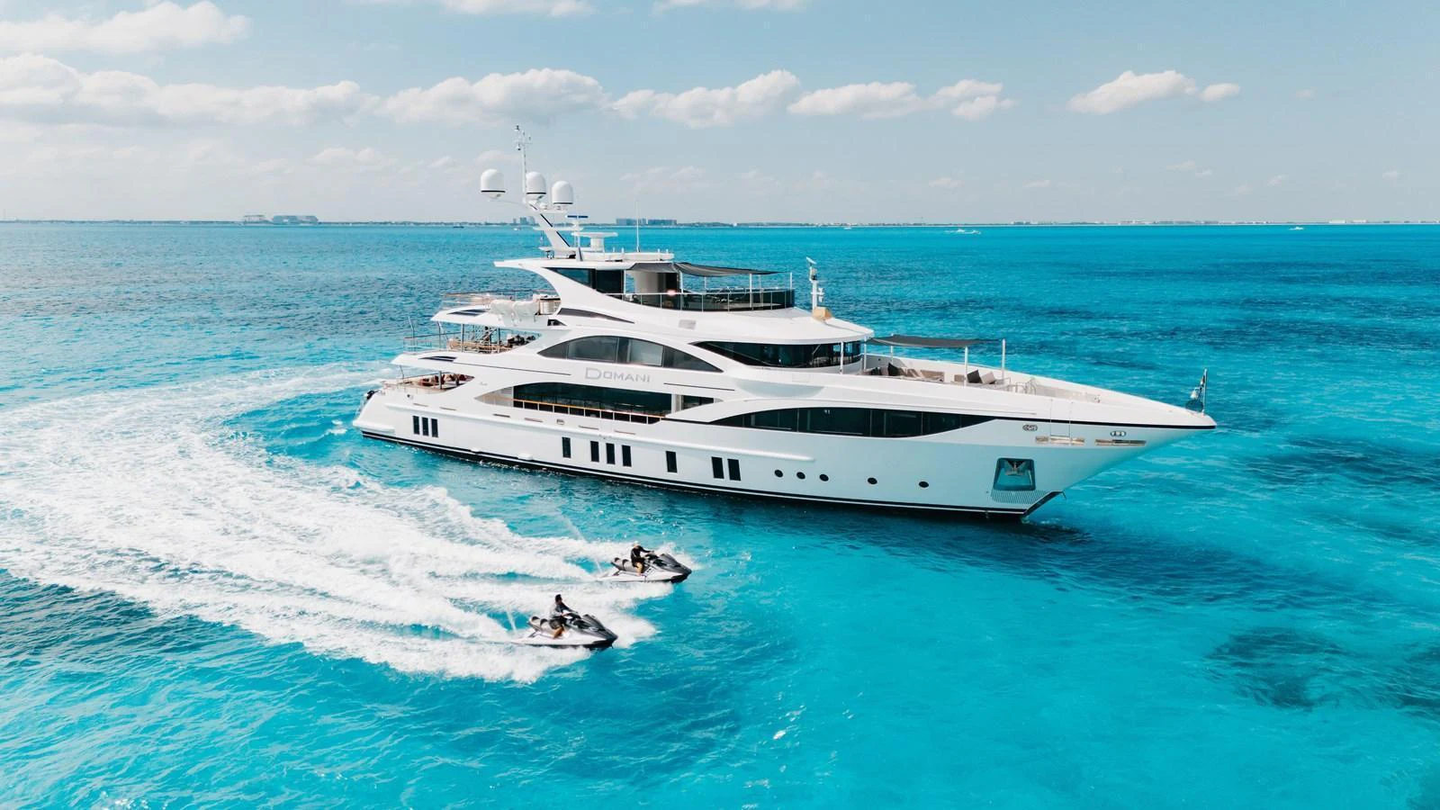 A luxurious yacht cruises through clear blue waters, accompanied by two jet skis. aboard DOMANI Yacht for Sale