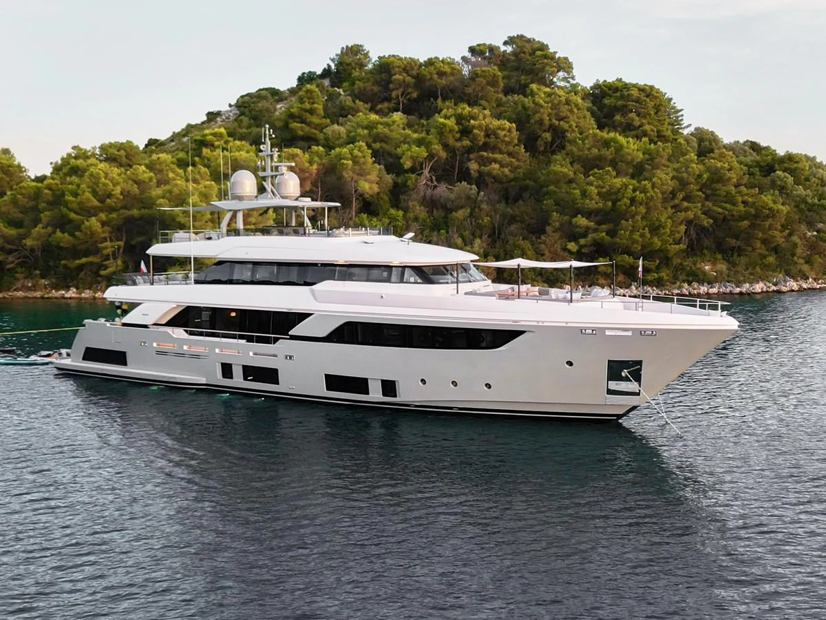 A sleek and modern yacht cruises gracefully along a scenic coastline with lush greenery in the background. aboard BIZMAN Yacht for Sale