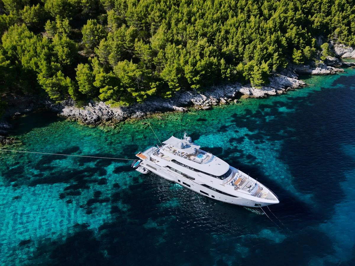 A luxurious yacht is anchored in a serene, turquoise bay surrounded by lush greenery. aboard BIZMAN Yacht for Sale