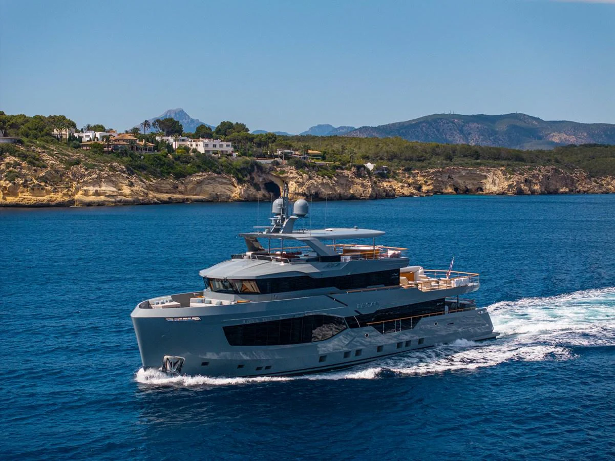 A luxurious yacht cruises through clear blue waters with a scenic coastal backdrop. aboard OSCAR Yacht for Sale