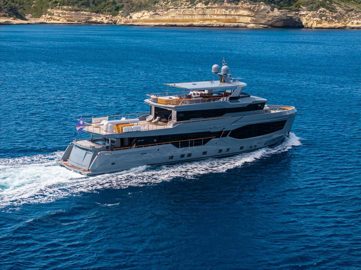 A luxurious yacht cruises through pristine blue waters with a scenic coastline in the background. aboard OSCAR Yacht for Sale